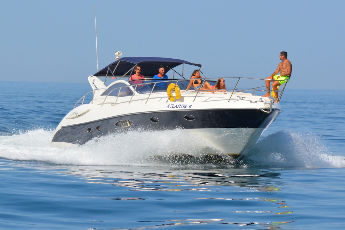 A boat filled with eager adventurers approaches the enchanting entrance of Benagil Cave, revealing the cave's majestic arch against the backdrop of the Algarve's crystal-clear waters