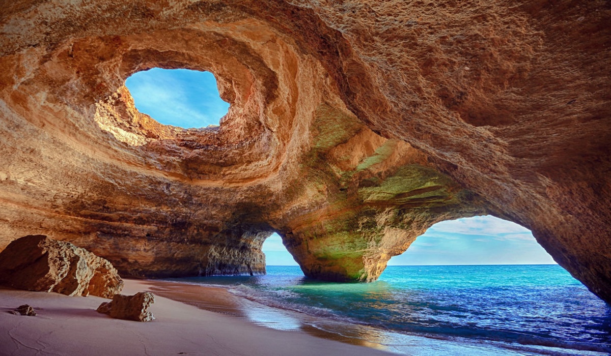 A boat filled with eager adventurers approaches the enchanting entrance of Benagil Cave, revealing the cave's majestic arch against the backdrop of the Algarve's crystal-clear waters