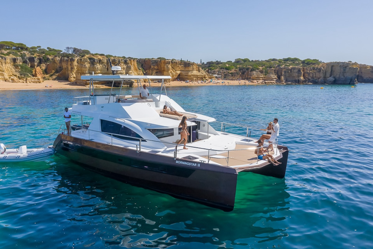 A boat filled with eager adventurers approaches the enchanting entrance of Benagil Cave, revealing the cave's majestic arch against the backdrop of the Algarve's crystal-clear waters