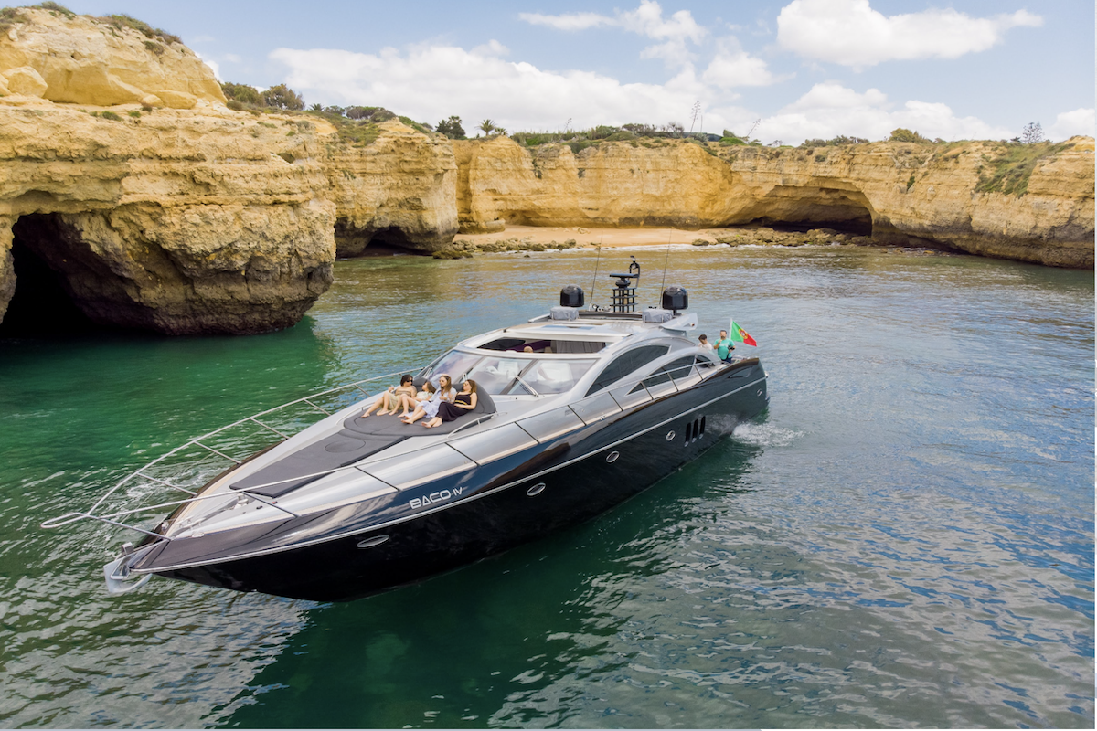 A boat filled with eager adventurers approaches the enchanting entrance of Benagil Cave, revealing the cave's majestic arch against the backdrop of the Algarve's crystal-clear waters