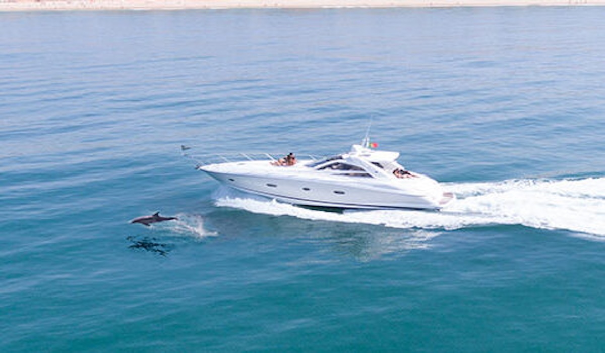 A boat filled with eager adventurers approaches the enchanting entrance of Benagil Cave, revealing the cave's majestic arch against the backdrop of the Algarve's crystal-clear waters